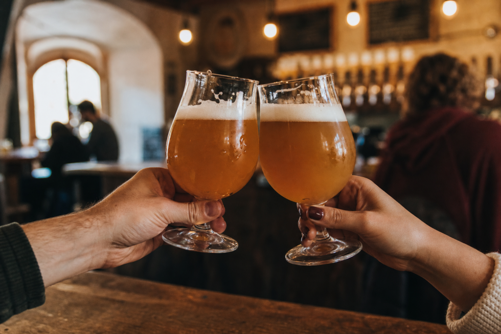 Due persone brindano con bicchieri di birra artigianale chiara e velata in una taproom calda e accogliente, una scena tipica dei birrifici artigianali del Veneto
